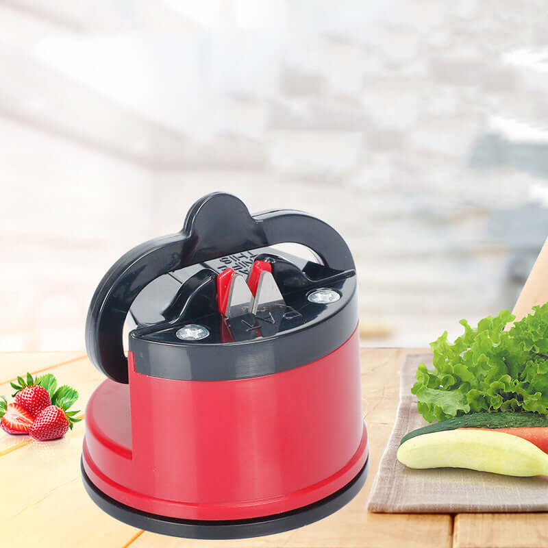 A red knife sharpener is placed on a kitchen counter next to fresh vegetables.